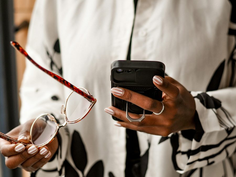 Hands holding a phone and reading glasses, examining the details